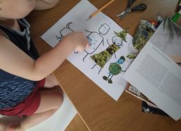 Przy stole dziecko wykonuje pracę, na stole papiery, gazety