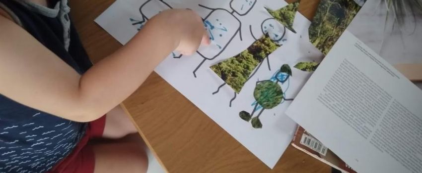 Przy stole dziecko wykonuje pracę, na stole papiery, gazety