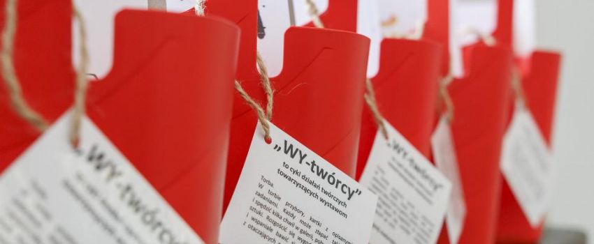 na parapecie stoi 5 czerwonych toreb z metkami WY-twórcy. W środku kartki