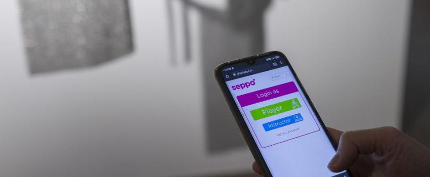 Na pierwszym planie dłonie trzymające smartfon. W tle srebrny obiekt