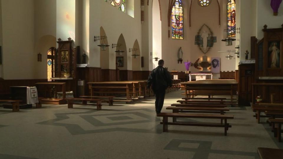 Widok wnętrza świątyni. Po obu stronach rzędy ławek. Pomiędzy nimi ubrany na czarno mężczyzna. Widać jego tył.