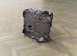 Prostopadłościenny blok z kawałków sprasowanego metalu na drewnianej podłodze.