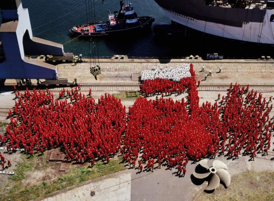 2 część dyptyku. Zdjęcie przedstawia kilka tysięcy żołnierzy, ubranych  w czerwone i białe bluzy. Tłum rozchodzi się w różnych kierunkach.  Dominuje czerwień. Rzecz dzieje się na betonowym nabrzeżu.