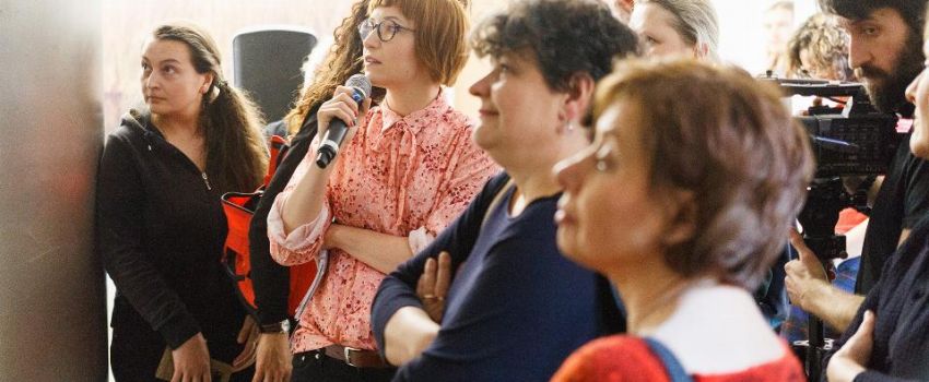 Na zdjęciu ludzie podczas oprowadzania po wystawie. Jedna z kobiet trzyma w dłoni mikrofon.