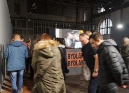 Ludzie ubrani w kurtki zwiedzają wystawę w hali starej elektrowni - budynku Galerii Arsenał