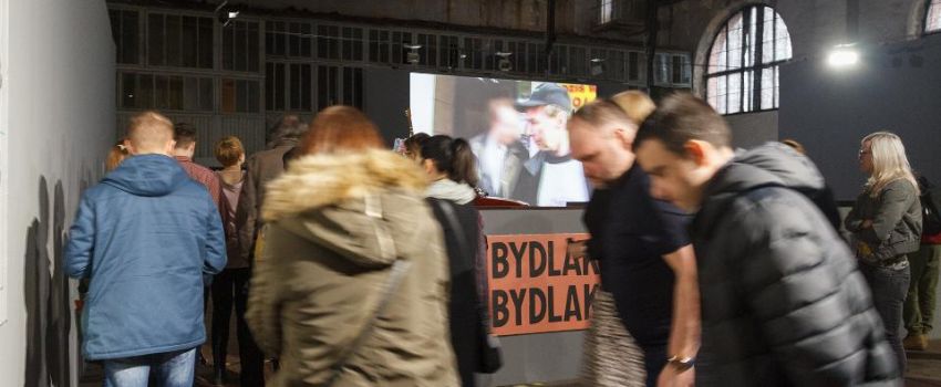 Ludzie ubrani w kurtki zwiedzają wystawę w hali starej elektrowni - budynku Galerii Arsenał