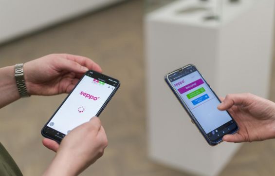 w centralnej części zdjęcia trzymane przez dwie różne osoby dwa telefony, na których widoczne jest logo gry SEPPO